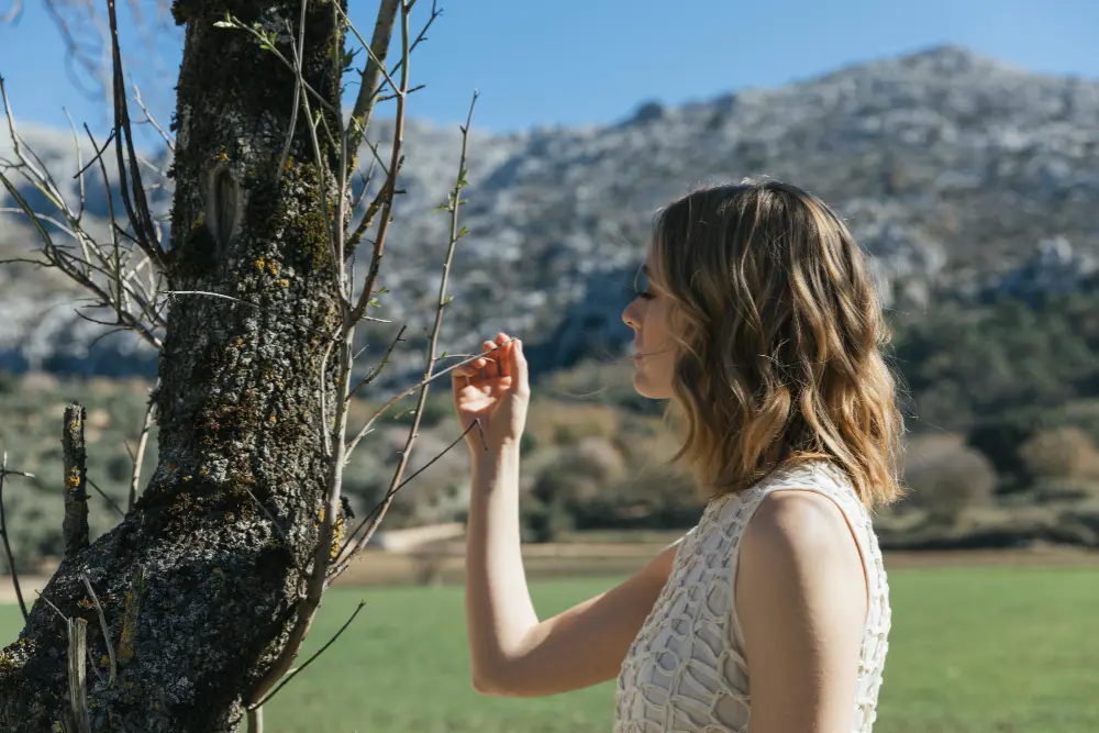 Kobieta w sukience bez rękawów dotyka gałęzi drzewa w malowniczym, górskim plenerze, odnajdując spokój przypominający psychoterapię Szczecin.