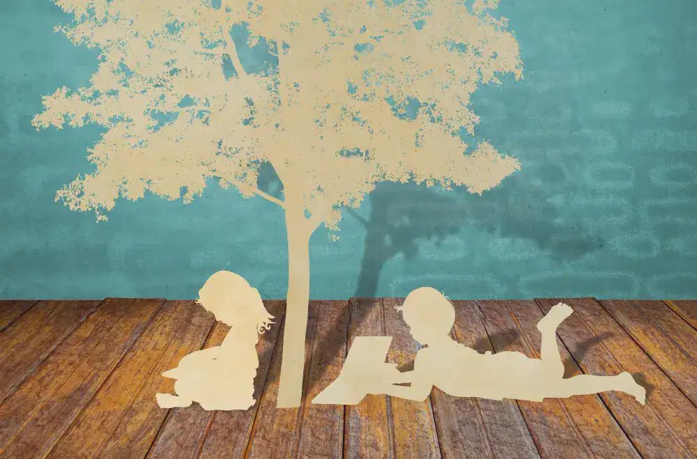 Papierowe wycinanki dwojga dzieci czytających pod drzewem na drewnianej podłodze z niebieskim tłem, przywołujące uspokajającą atmosferę często poszukiwaną podczas sesji psychoterapii Szczecin.